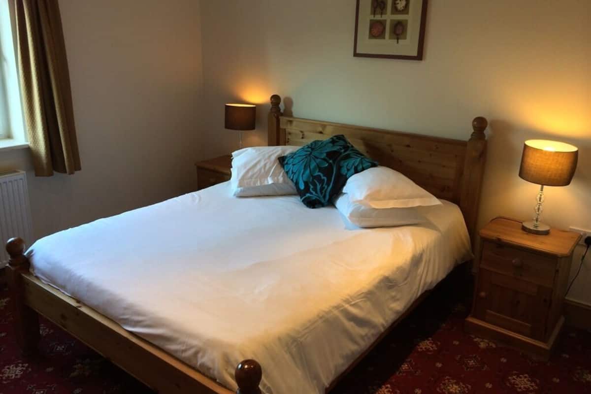 A neatly made bed with white linens and a teal pillow, flanked by two bedside lamps on wooden nightstands.