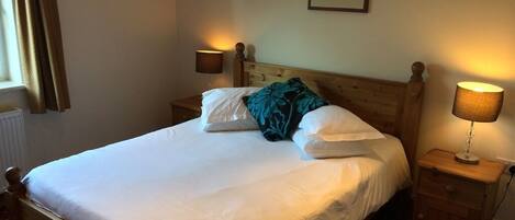 A neatly made bed with white linens and a teal pillow, flanked by two bedside lamps on wooden nightstands.