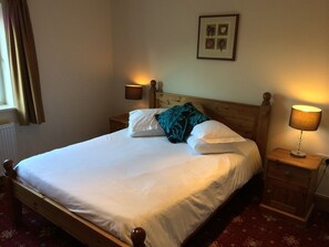 A neatly made bed with white linens and a teal pillow, flanked by two bedside lamps on wooden nightstands.