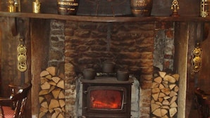 A rustic stone fireplace with a wood-burning stove, stacked firewood, and decorative items on shelves above. - Hunters Lodge Inn (Wincanton)