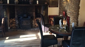 A cozy dining area with a stone fireplace, wooden flooring, and black upholstered chairs. - Hunters Lodge Inn (Wincanton)