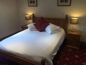A neatly made bed with white linens and a red pillow, flanked by two bedside tables with lamps, in a room with a patterned carpet.