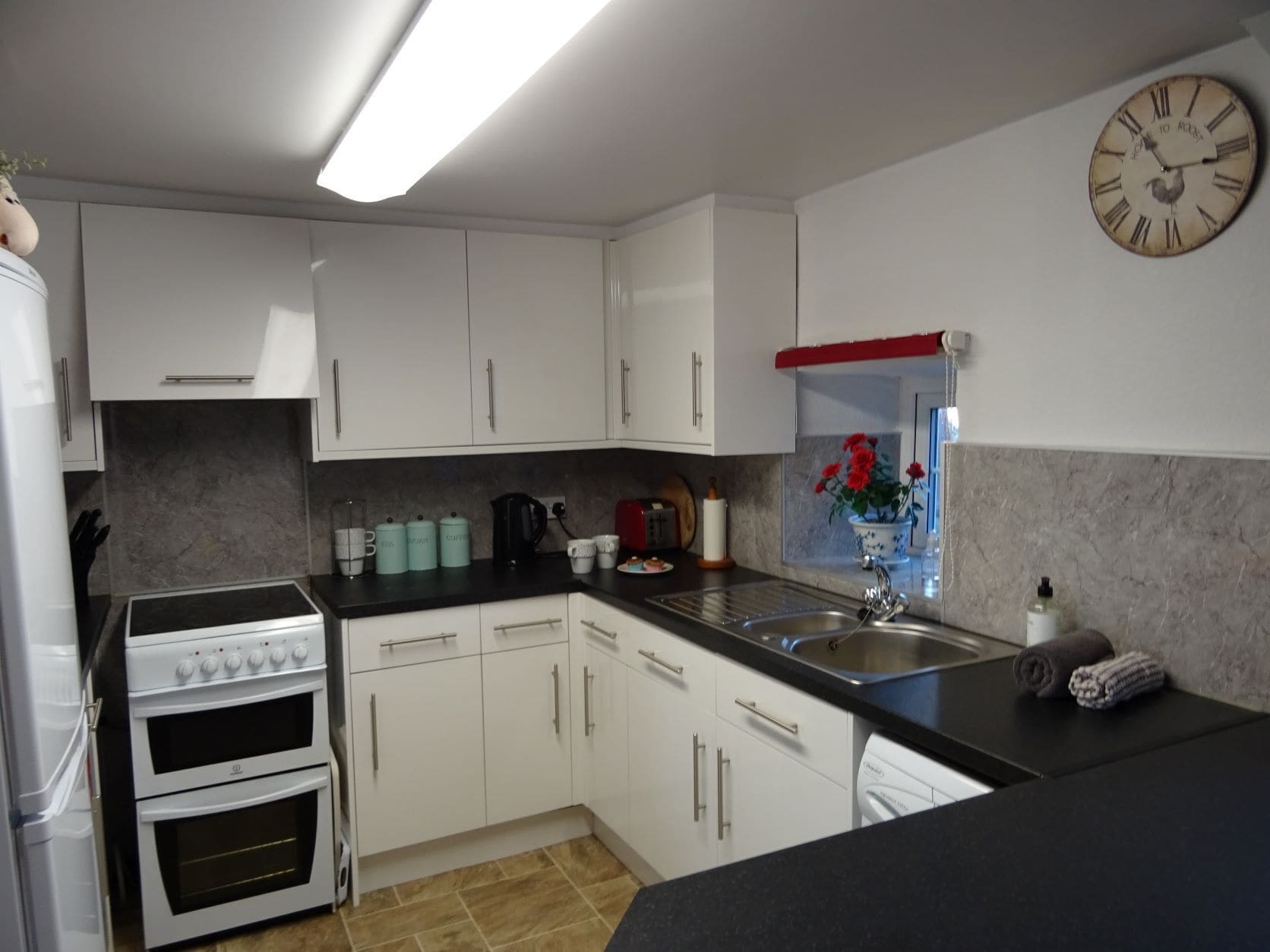 A modern kitchen with white cabinets, a black countertop, a built-in oven, a sink, and a clock on the wall.