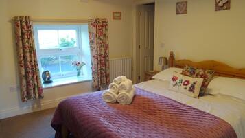 Un dormitorio con cama, ventana con cortinas, radiador y mesita de noche con lámpara.
