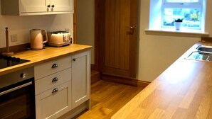 Una cucina con pavimento in legno, mobili bianchi, forno integrato, un tostapane e una finestra con vista.