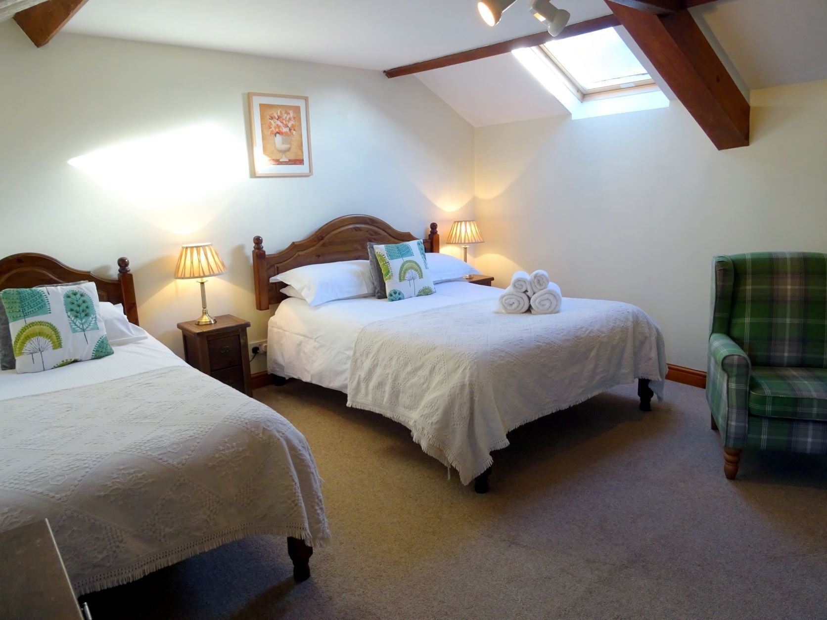Ein Schlafzimmer mit zwei Betten, einem grünen Karo-Sessel und einem Dachfenster.