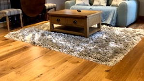 Un soggiorno con un tavolino in legno, un divano grigio con cuscini decorati, una poltrona a quadri, una lampada e una scala sullo sfondo.