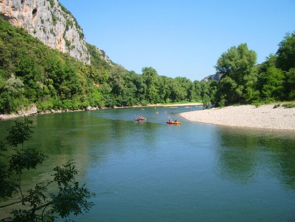 Un río tranquilo con kayaks, rodeado de abundante vegetación y un risco rocoso.