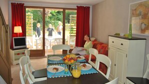 Un comedor con una mesa para dos personas, un televisor y vista al jardín a través de la puerta corrediza de vidrio.