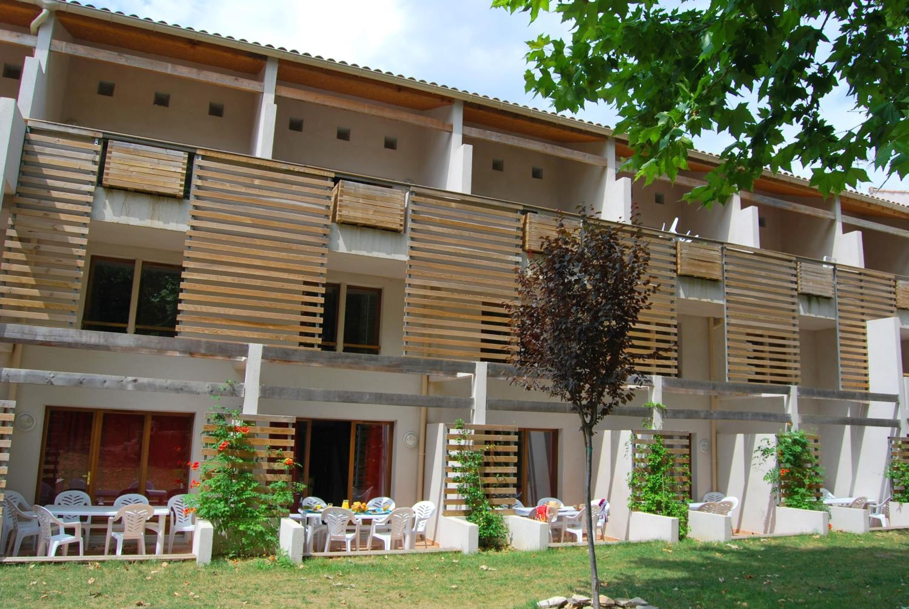 A multi-story hotel with balconies, outdoor seating areas, and a small tree in the foreground.