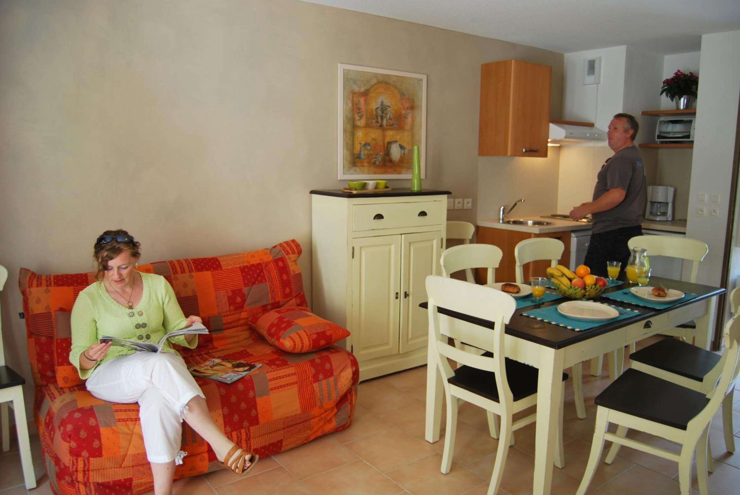 Un saló amb un sofà, una taula de dinar amb cadires, i una cuina amb armaris i electrodomèstics.