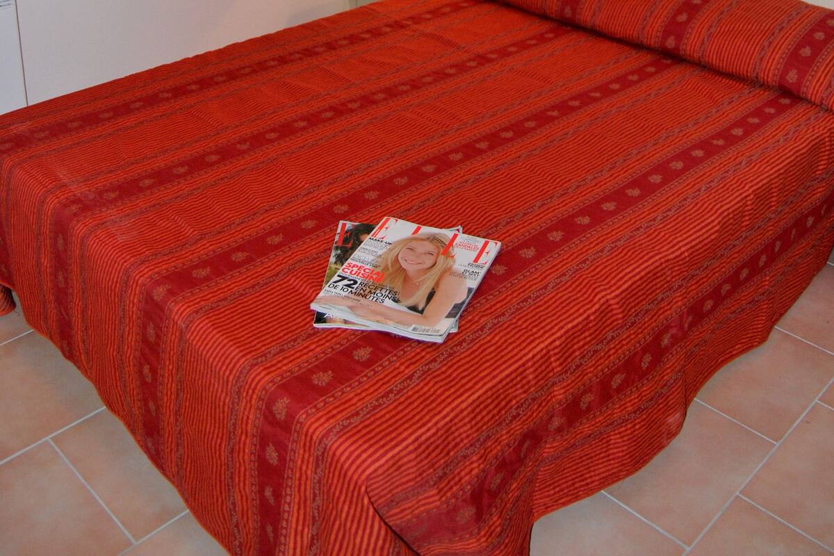Una cama bien hecha con un edredón rojo, una lámpara de noche y una revista sobre la cama.