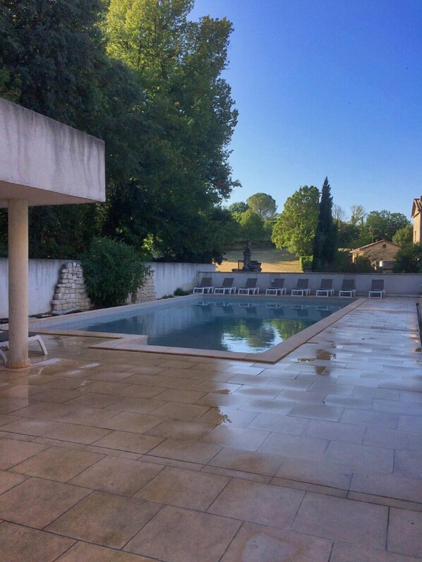 Una piscina rectangular con un borde empinado y azulejado, rodeada de árboles y un muro de piedra.
