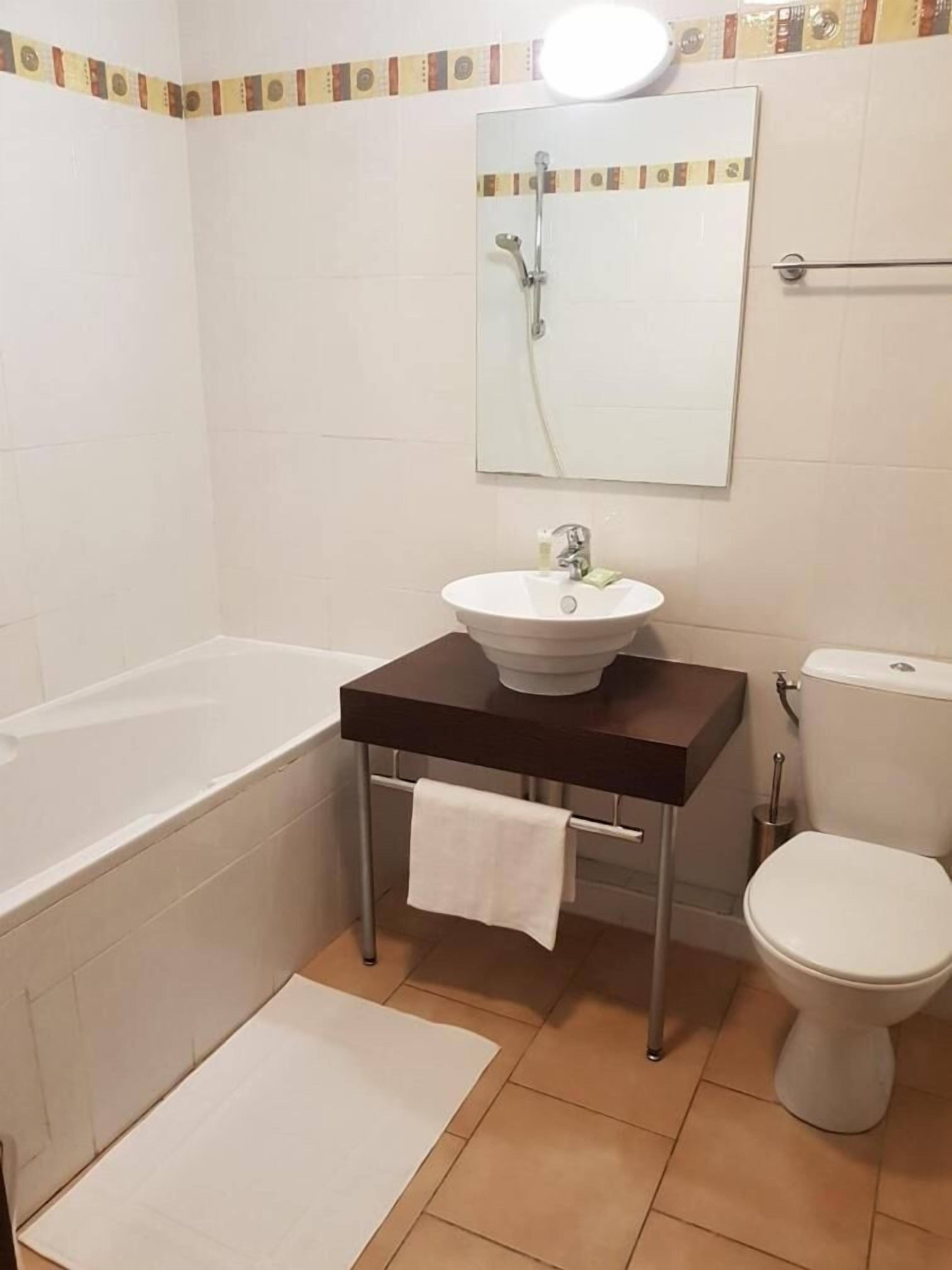 Et badeværelse med badekar, håndvask, toilet og et spejl over håndvasken.