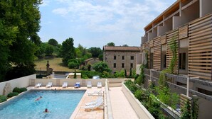Una piscina con sillas de descanso, un edificio de piedra y follaje al fondo.