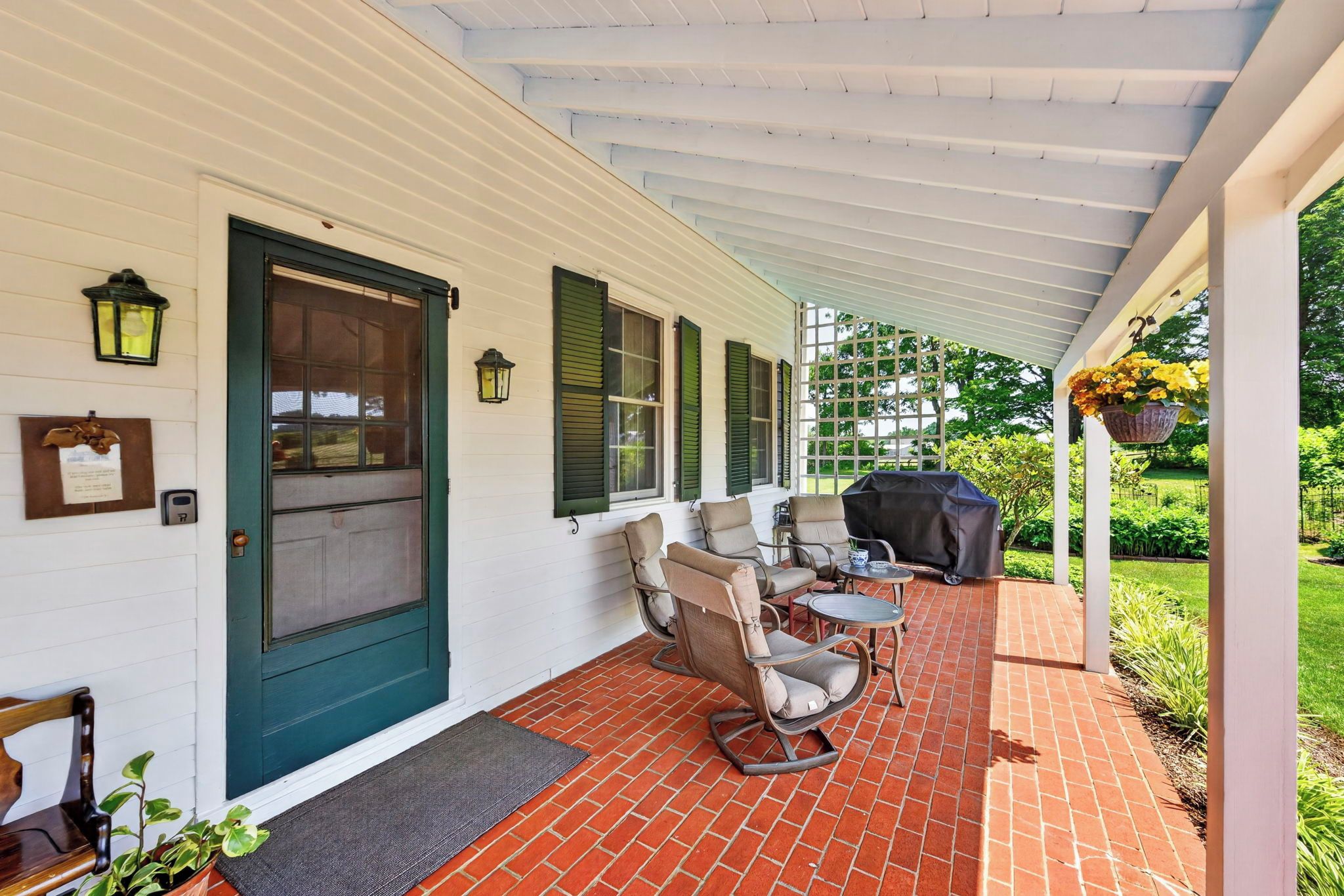 A covered porch with outdoor furniture, a grill, and a door with shutters.