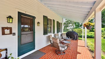 A covered porch with outdoor furniture, a grill, and a door with shutters.