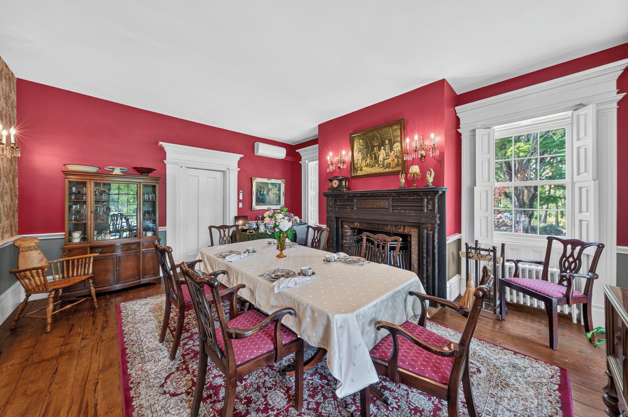 A dining room with a large table, chairs, a fireplace, and a window with a view.
