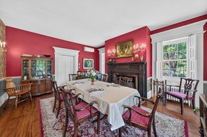 A dining room with a large table, chairs, a fireplace, and a window with a view. - The Neighbour House B&B (Long Valley)