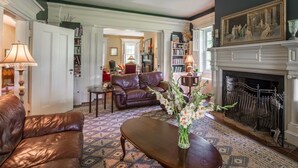 A traditional living room with a fireplace, leather sofa, and a patterned rug. - The Neighbour House B&B (Long Valley)