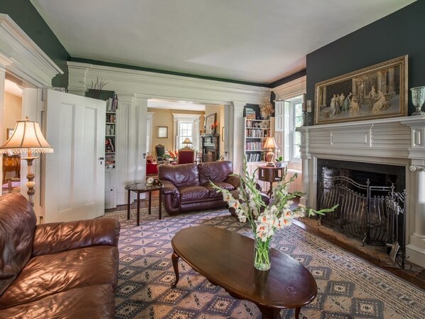 A traditional living room with a fireplace, leather sofa, and a patterned rug. - The Neighbour House B&B (Long Valley)