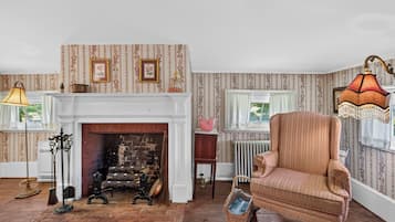 Een kamer met een open haard, een antieke fauteuil en behang met een patroon.
