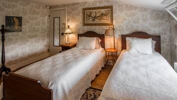 Un dormitorio con dos camas de madera, una mesita de noche con una lámpara, un espejo y un cuadro con motivos florales en la pared.