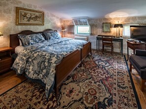 A bedroom with a wooden bed, a desk, a chair, a television, and a radiator.