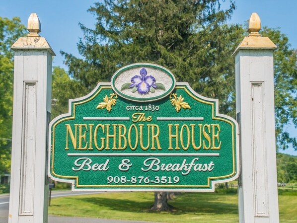 A green sign with gold lettering for The Neighbour House Bed & Breakfast, including a phone number.