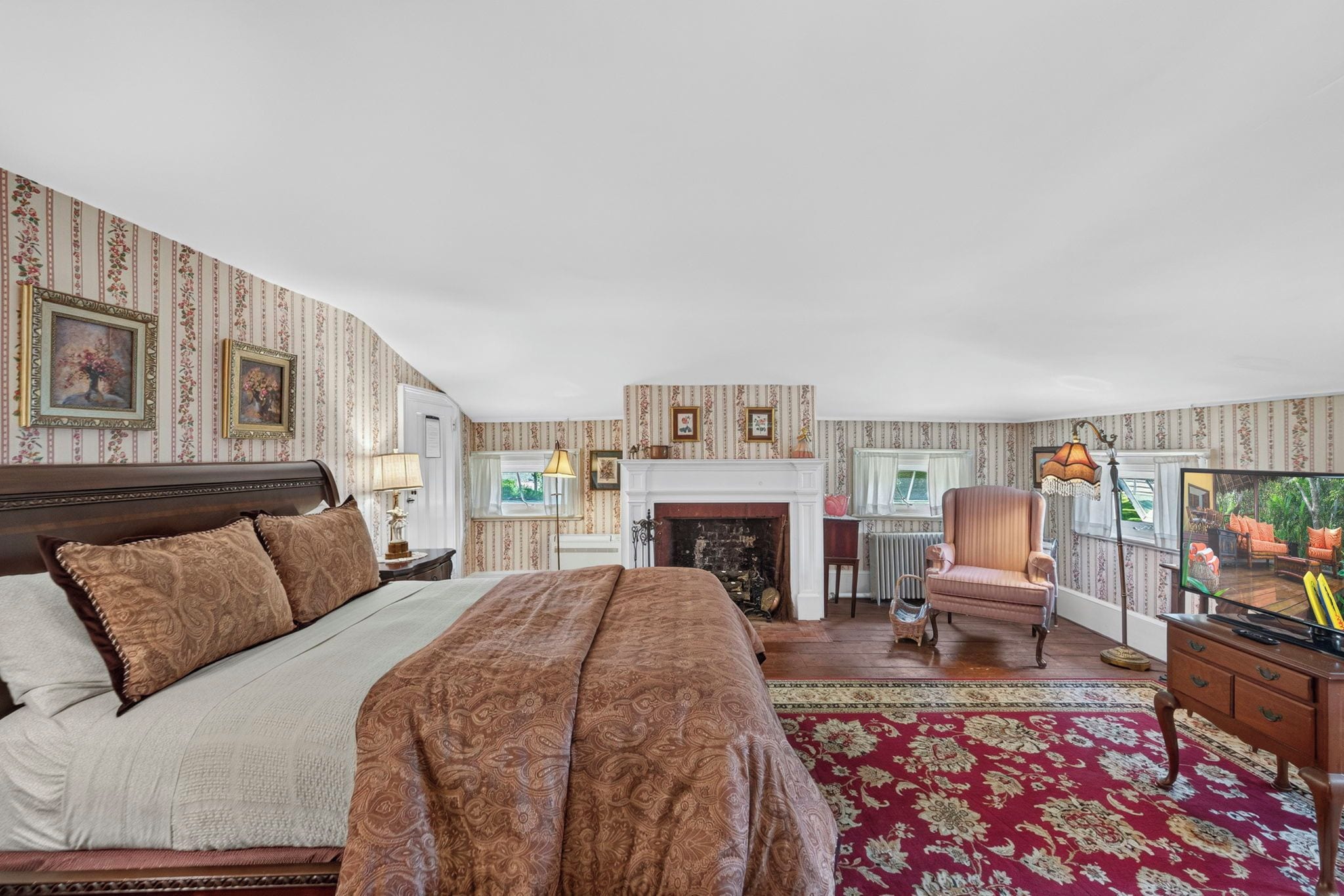 A bedroom with a large bed, a fireplace, a sitting area with a chair, and a television.