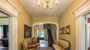 A hallway with a chandelier, framed artwork, and a staircase leading to another room. - The Neighbour House B&B (Long Valley)