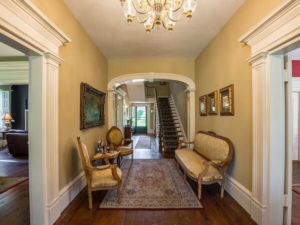 A hallway with a chandelier, framed artwork, and a staircase leading to another room. - The Neighbour House B&B (Long Valley)