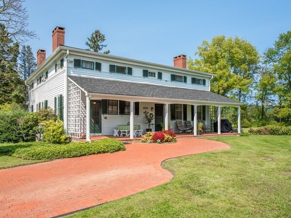 A two-story house with a covered porch, brick pathway, and landscaped garden. - The Neighbour House B&B (Long Valley)