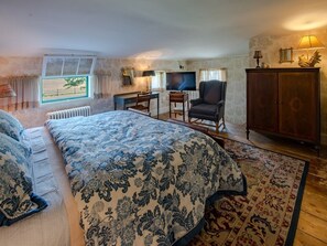 A bedroom with a large bed, a desk with a chair, a television, and a cabinet.