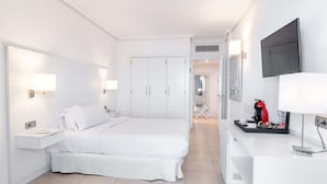 Quarto de hotel moderno com uma cama grande, mesas de cabeceira, uma escrivaninha com cafeteira e uma televisão de tela plana na parede.
