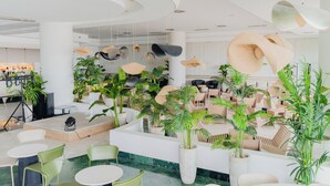 Um espaço interior moderno com mesas redondas, cadeiras verdes e plantas em vasos.