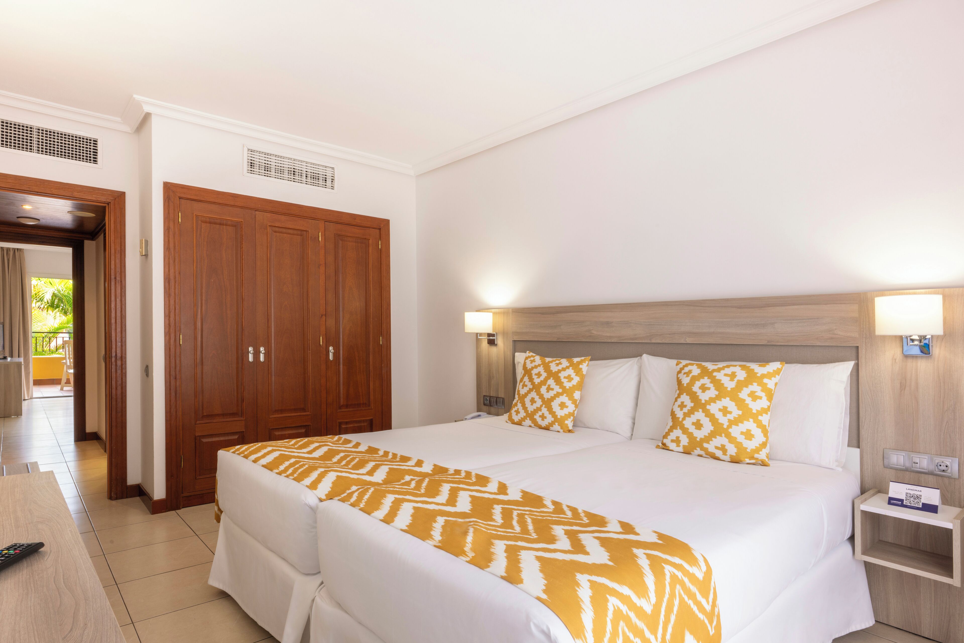 A hotel room with a large bed, two bedside tables, a wardrobe, and a bathroom visible through an open door.