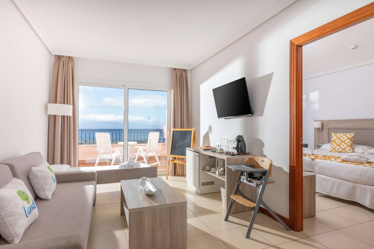 Une chambre d’hôtel avec un canapé, un bureau, une télévision, un lit et un balcon donnant sur la mer.