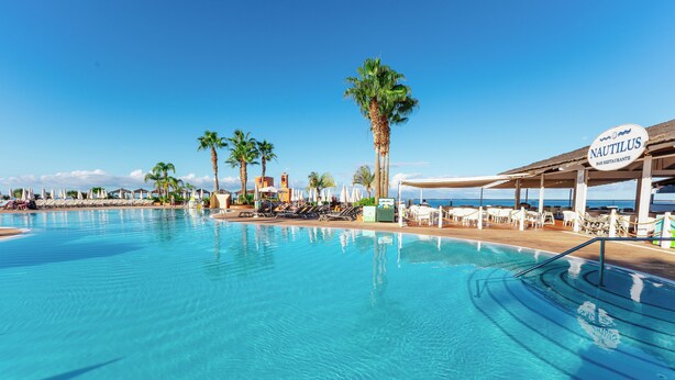 Uma área de piscina com espreguiçadeiras, guarda-sóis e uma placa indicando 'NAUTILUS Bar Restaurante'.