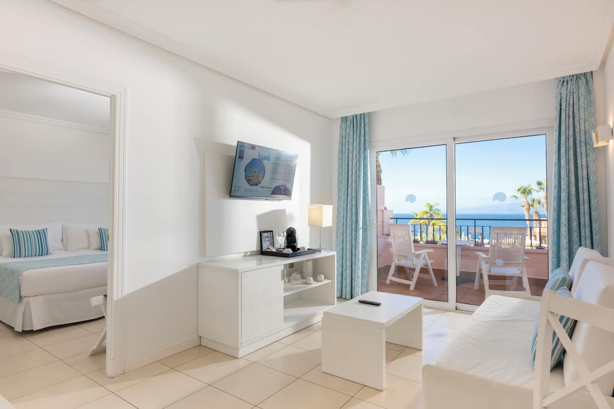 Une chambre d’hôtel avec un lit, un bureau, une télévision et un balcon donnant sur la mer.