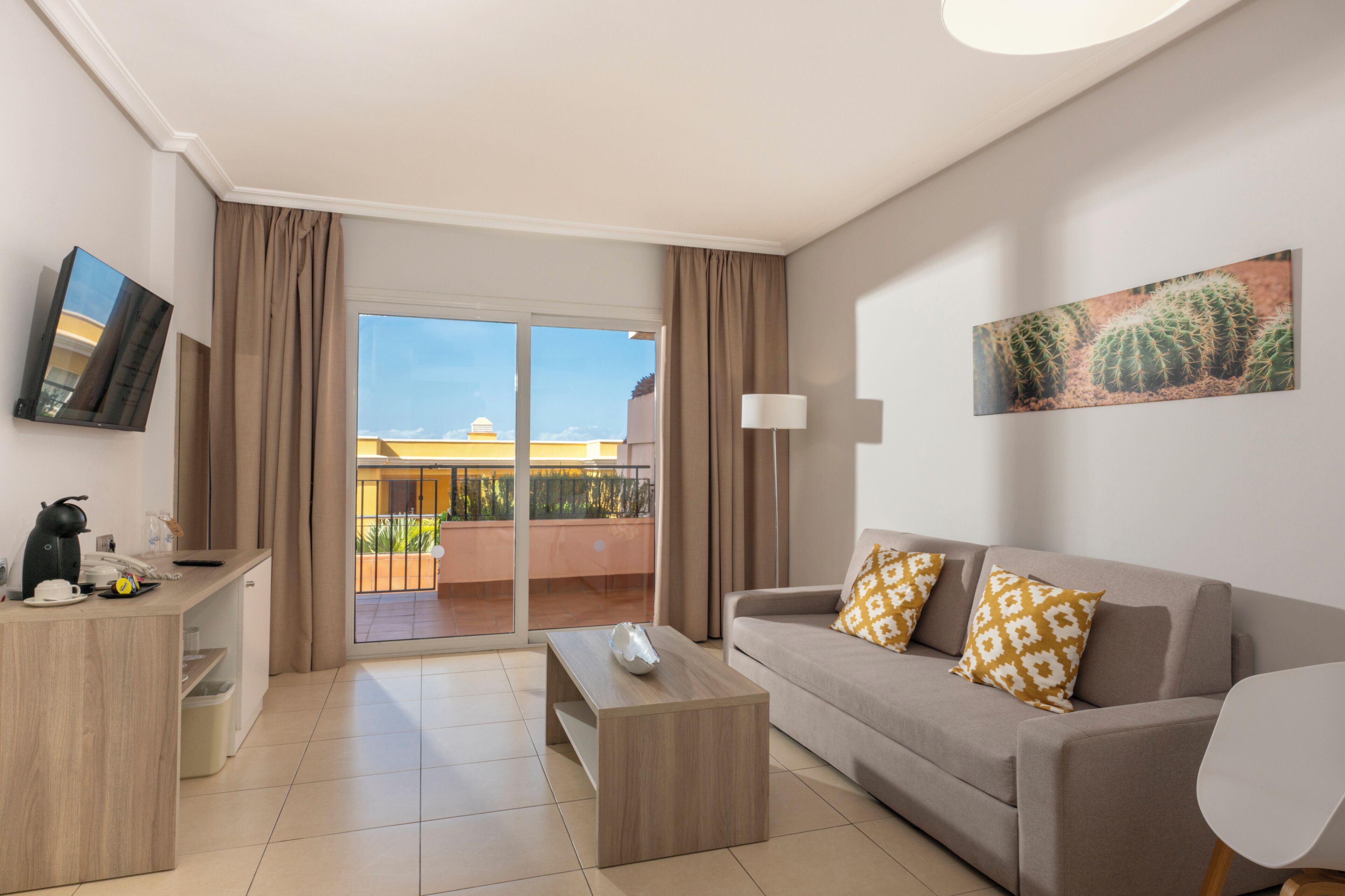 A modern hotel room with a sofa, coffee table, TV, and a balcony with a view.