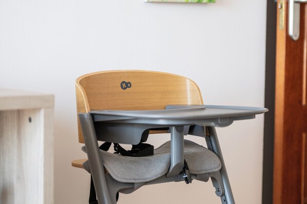 A high chair with a tray table, a wooden backrest, and a grey seat cushion.