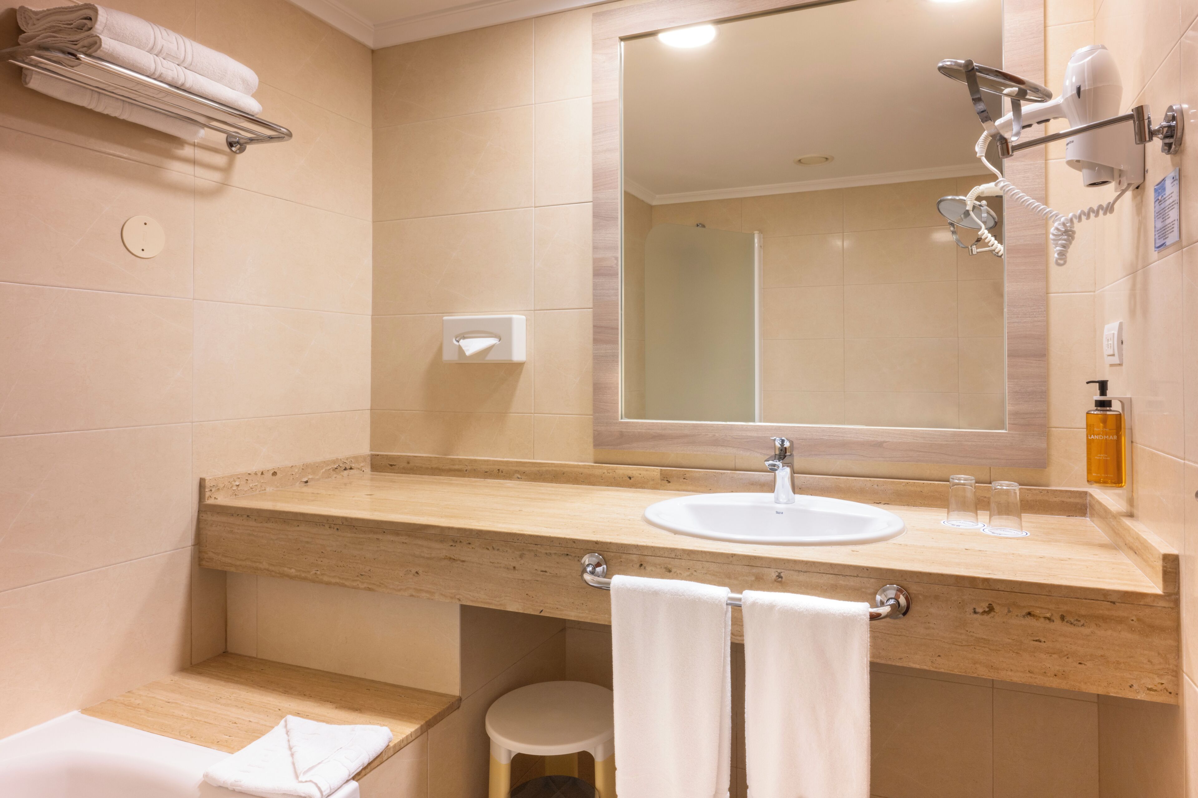 A bathroom with a sink, mirror, towel rack, and a handheld hair dryer.