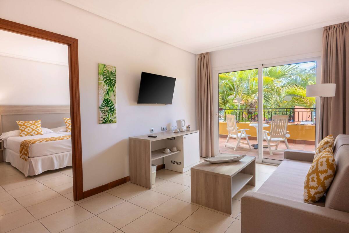Une chambre d’hôtel comprenant un lit, un canapé, une télévision, un bureau et un balcon avec des chaises.