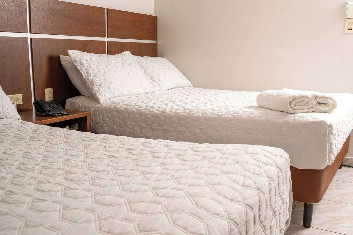 Hotellihuone, jossa on kaksi sänkyä, puinen pääty, taulu seinällä ja puhelin yöpöydällä.