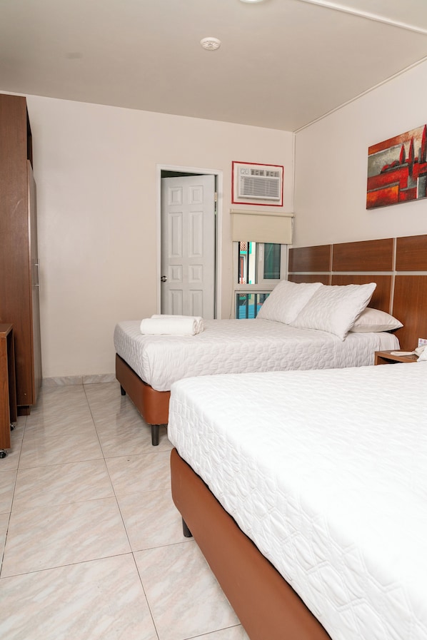 A hotel room with two beds, a wooden wardrobe, a door, a window, and a painting on the wall. - Hotel Benidorm Panama (Panama City)