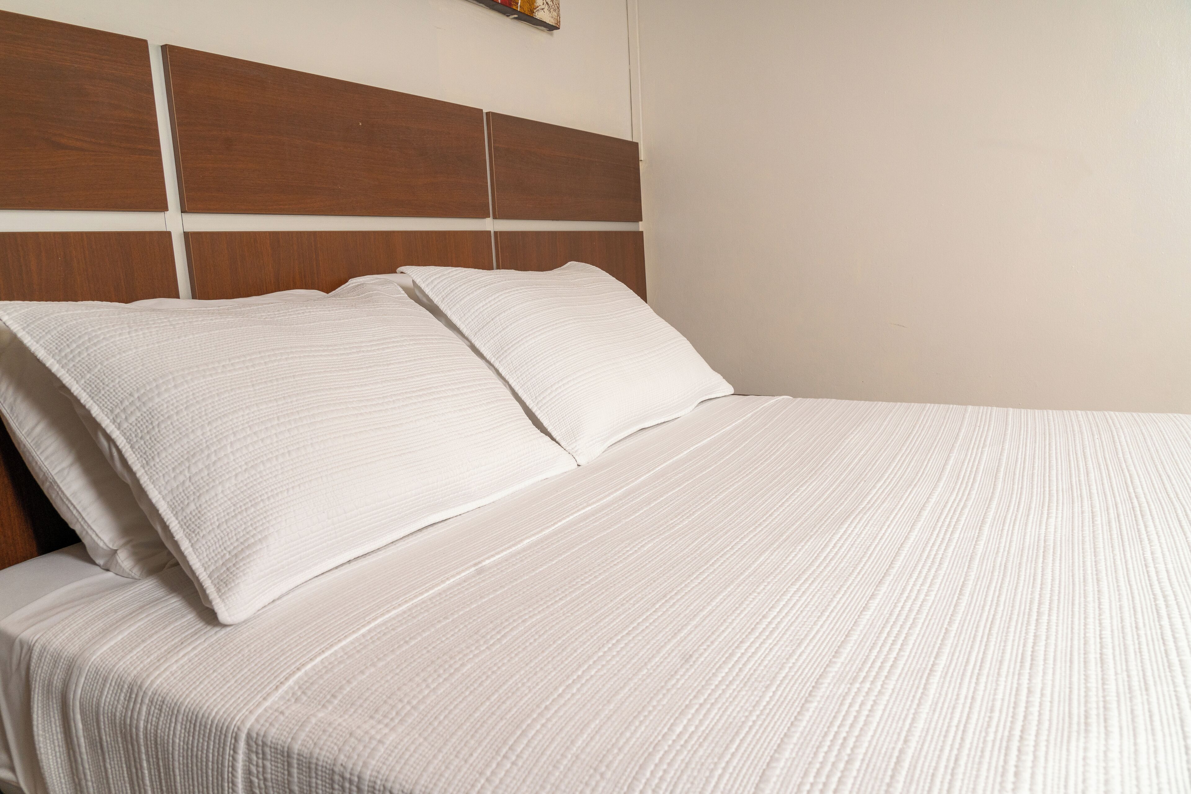 Una cama bien hecha con cabecera de madera y ropa blanca.