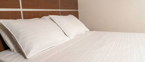 Una cama bien hecha con cabecera de madera y ropa blanca.