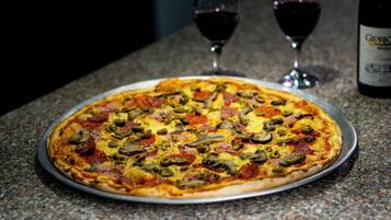 Pizza em uma bandeja de metal sobre uma bancada de granito, com duas taças de vinho e uma garrafa ao fundo.