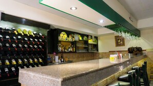 Zona de bar con un botellero, estantes con botellas, copas y un mostrador con taburetes.